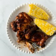 baked bbq chicken with a fork and corn on the cob on a white plate.