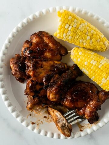 baked bbq chicken with a fork and corn on the cob on a white plate.