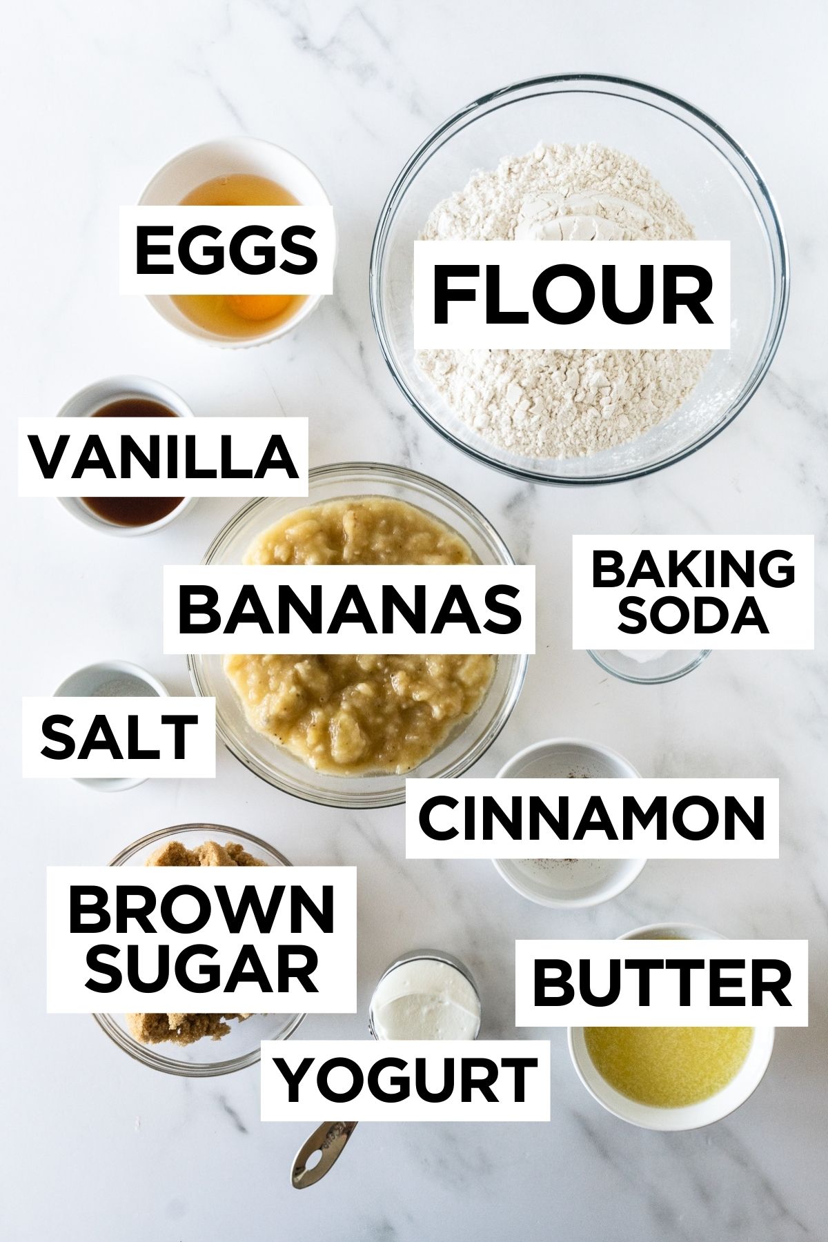 ingredients for banana bread in bowls on a white table.