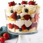 berry trifle in a glass trifle dish with pound cake, cheesecake filling, berries and whipped cream with text overlay.