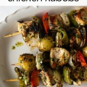cooked chimichurri chicken on skewers with potatoes and vegetables on a white platter.