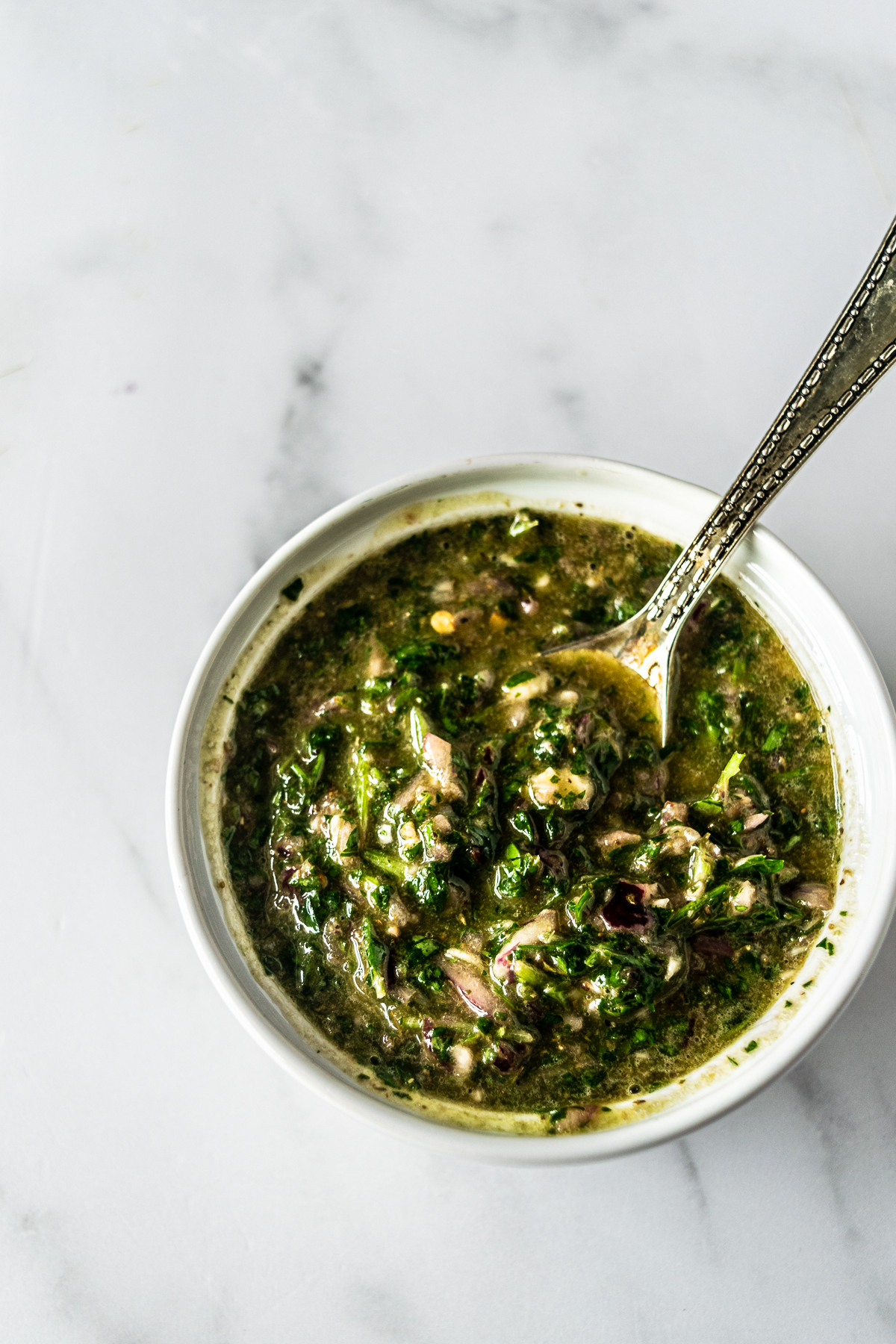 Argentinian chimichurri sauce in a white bowl with a spoon.