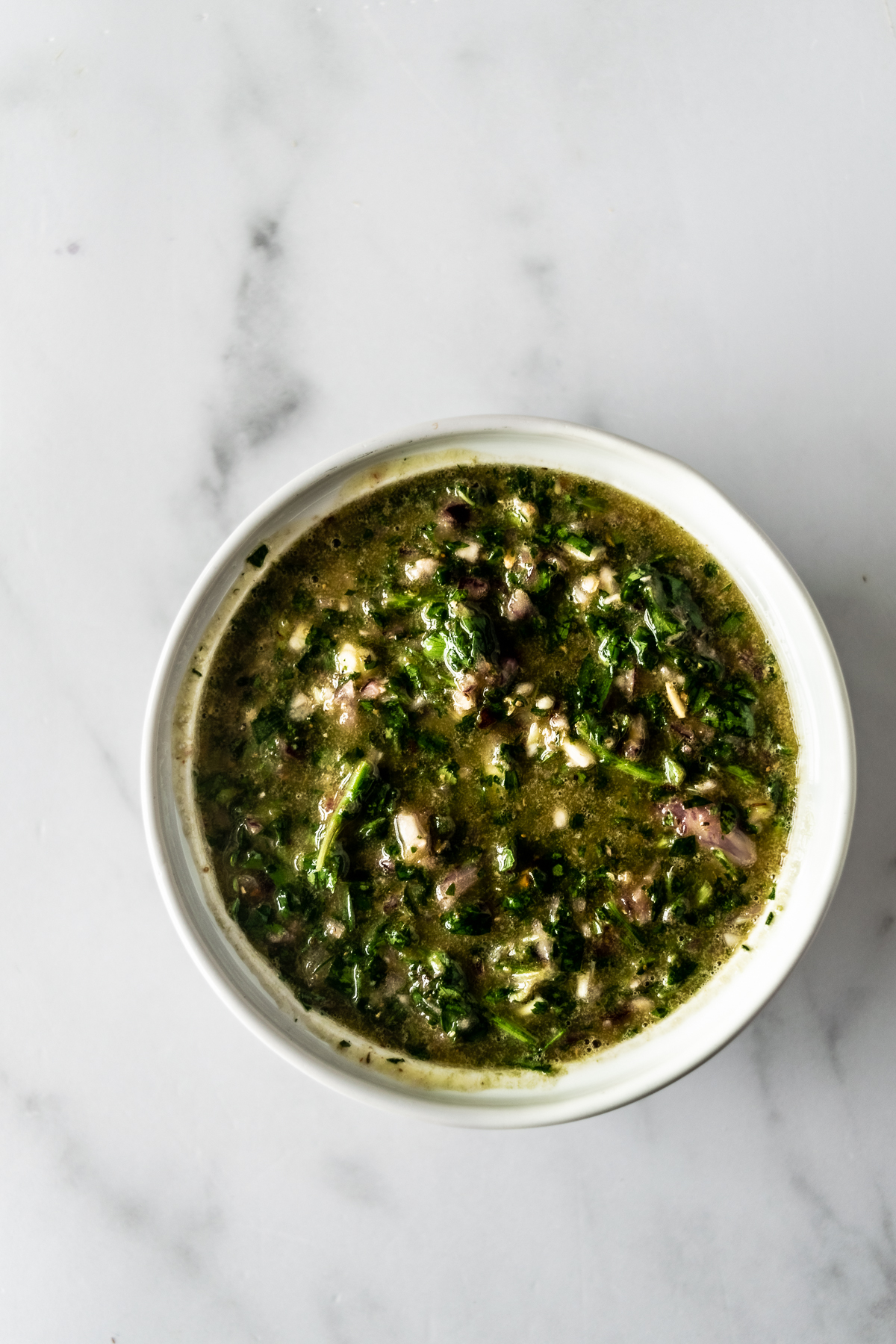 Argentinian chimichurri sauce in a white bowl with a spoon.