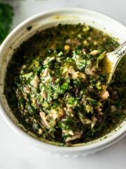 Argentinian chimichurri sauce in a white bowl with a spoon.
