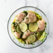 cilantro lime chicken marinade in a clear bowl topped with limes on a white table.