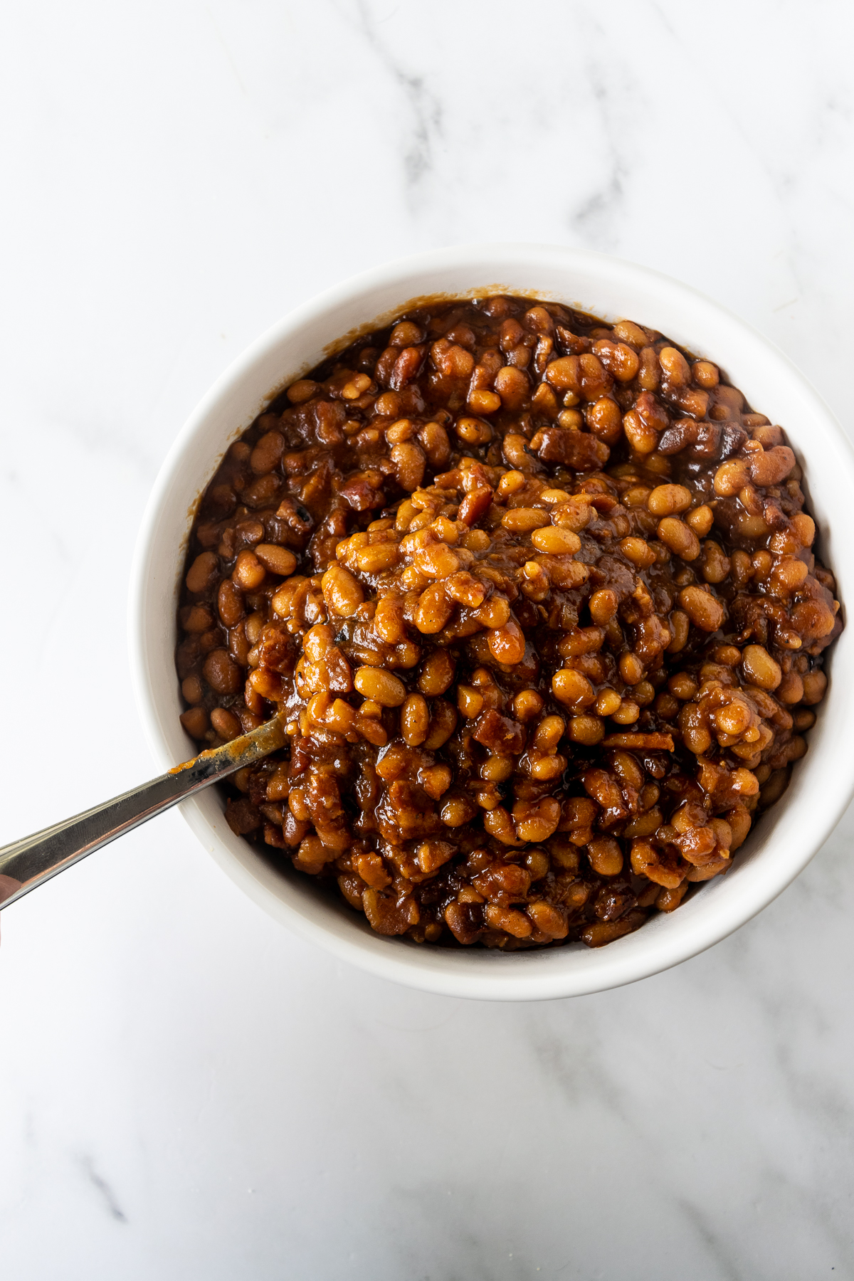 baked beans recipe in a white bowl with a spoon.