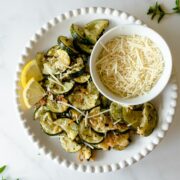 oven roasted zucchini slices on a white plate topped with parmesan cheese and lemon slices.