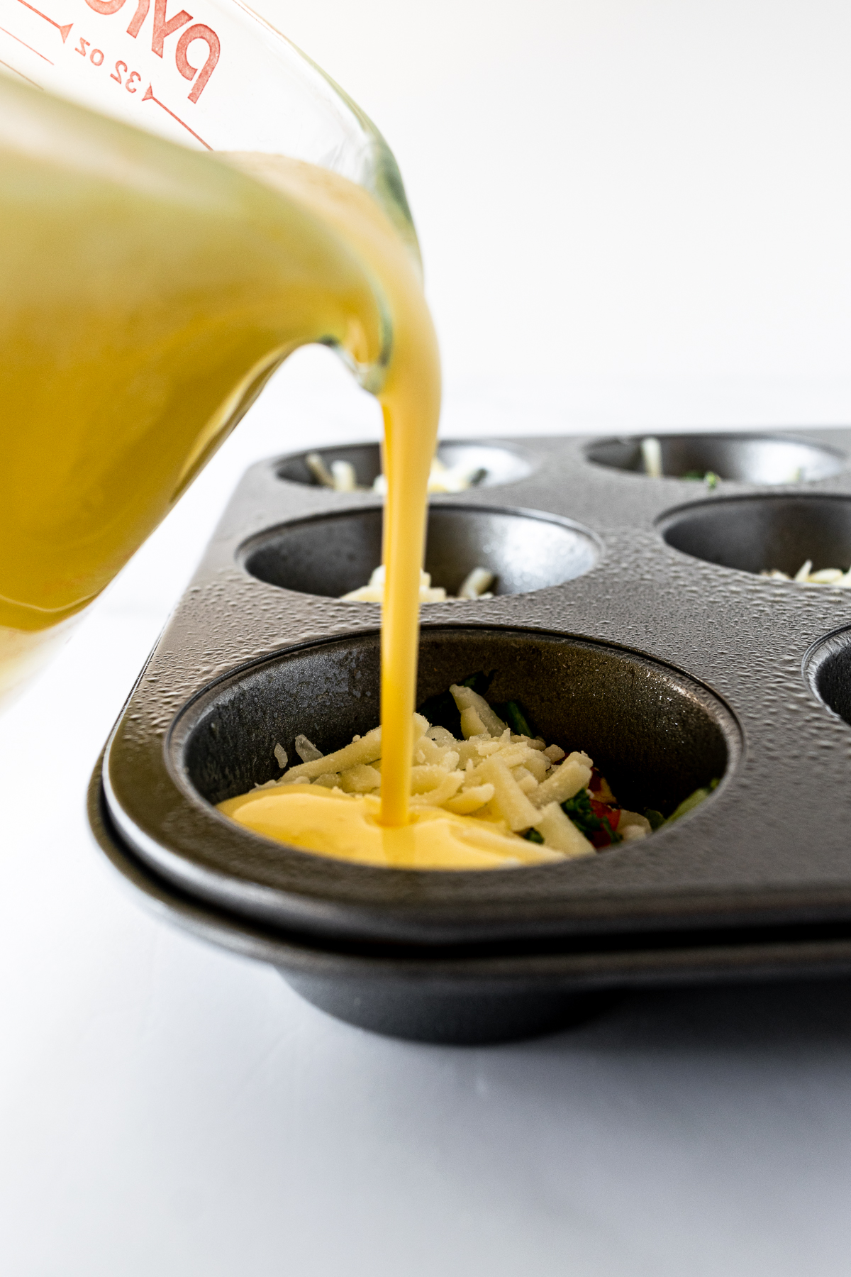 pouring egg muffin mixture into muffin tins.