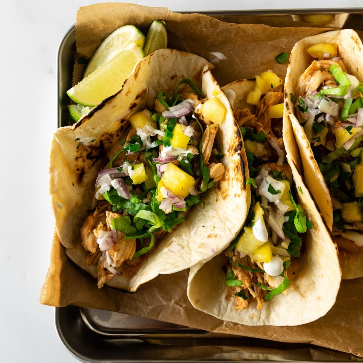 hawaiian chicken tacos on a tray topped with pineapple salsa.