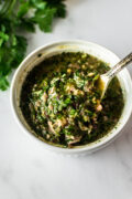 Argentinian chimichurri sauce in a white bowl with a spoon.