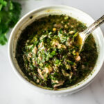 Argentinian chimichurri sauce in a white bowl with a spoon.