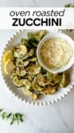 oven roasted zucchini slices on a white plate topped with parmesan cheese and lemon slices.