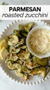 oven roasted zucchini slices on a white plate topped with parmesan cheese and lemon slices.