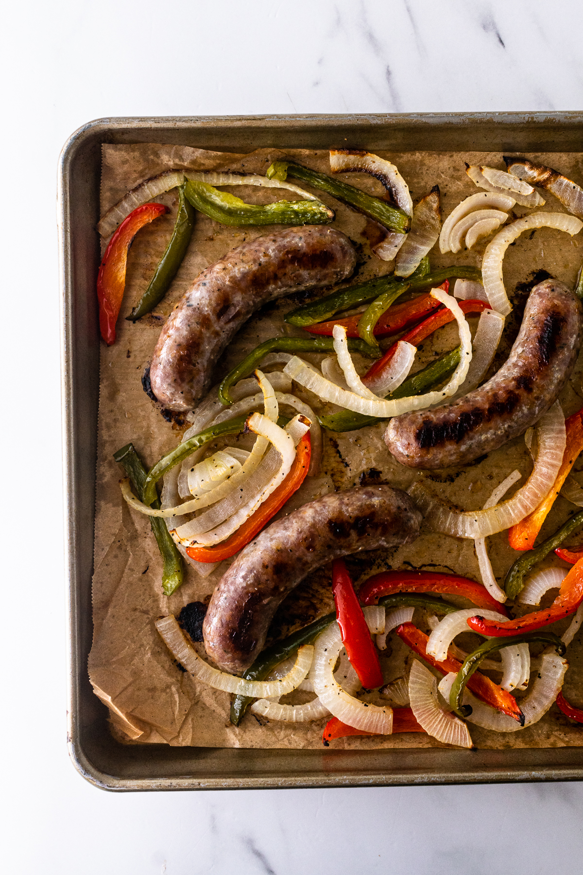 cooked Italian sausage and peppers on a sheet pan.