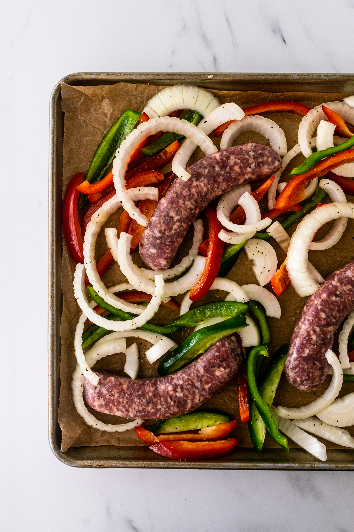 uncooked Italian sausage and peppers on a sheet pan.