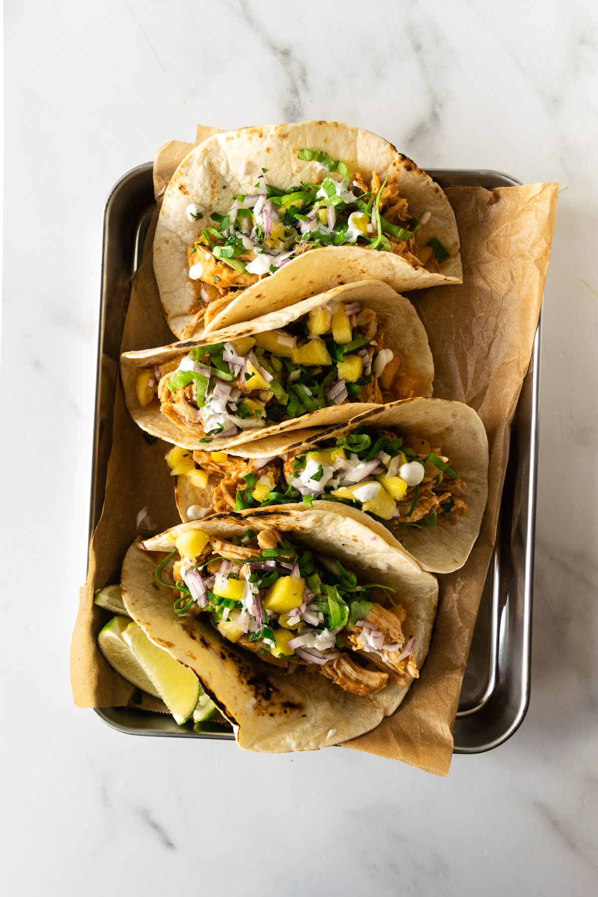 hawaiian chicken tacos on a tray topped with pineapple salsa.