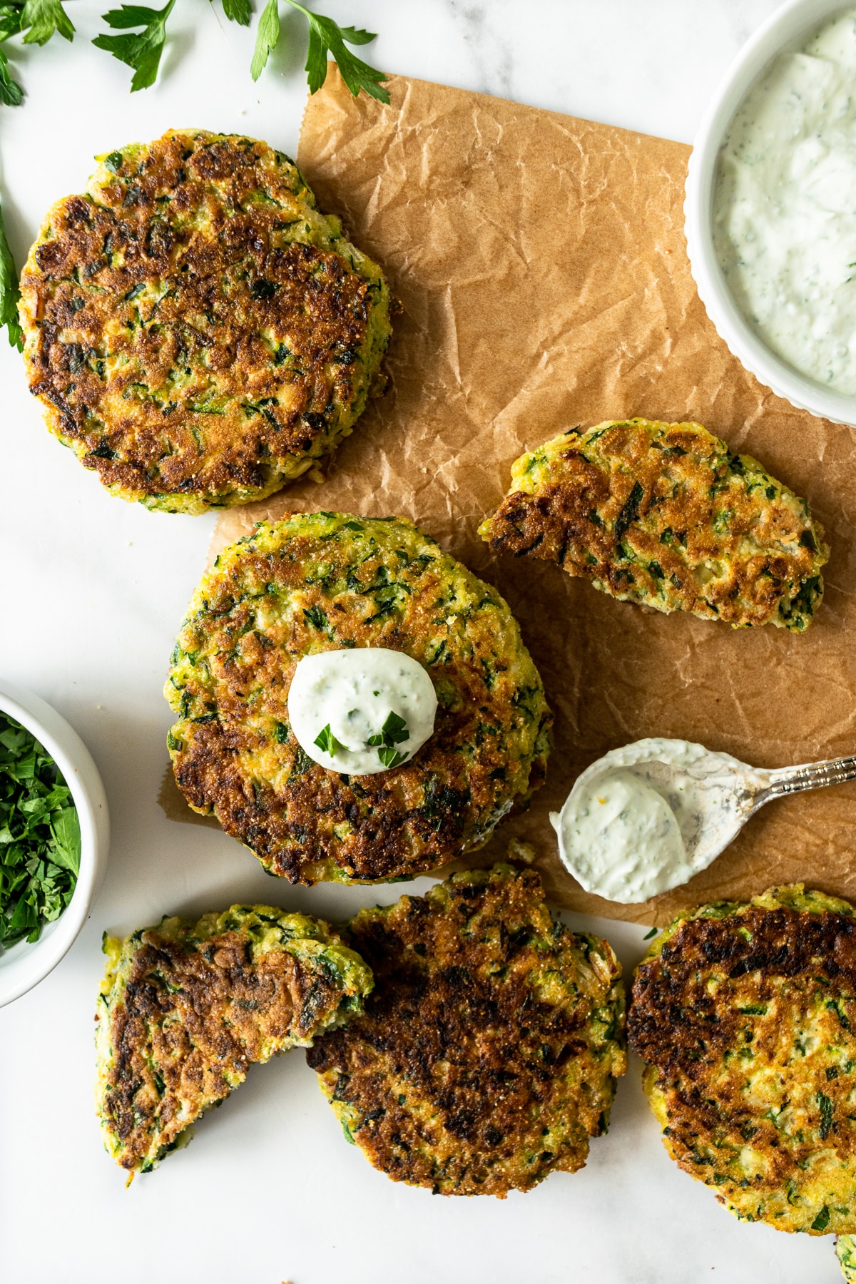 zucchini fritters on parchment paper topped with yogurt sauce.