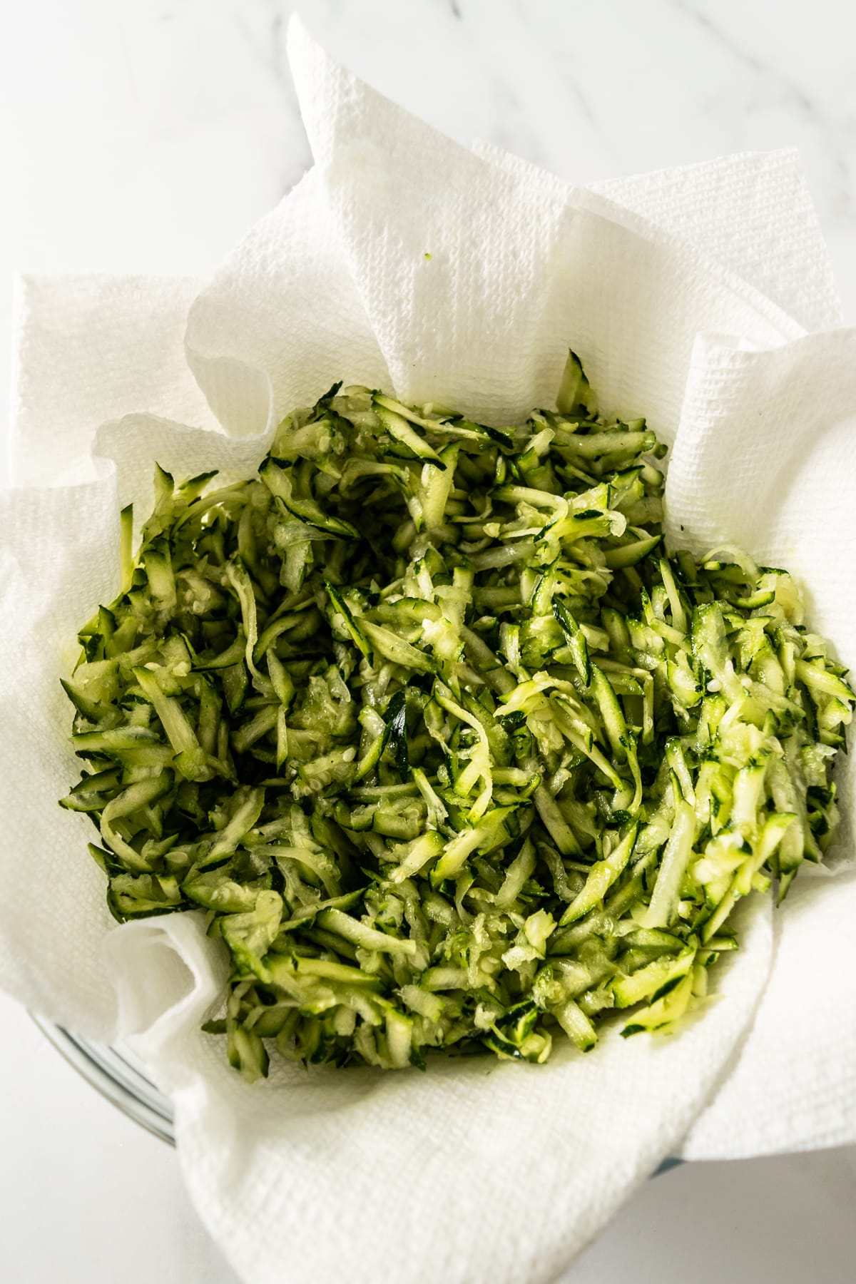 shredded zucchini in a paper towel-lined bowl.
