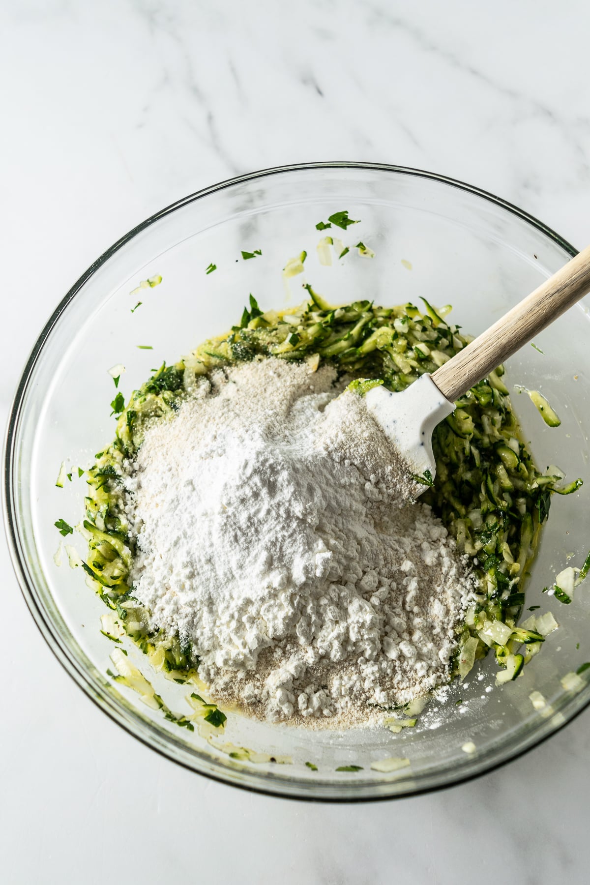 zucchini, cornmeal, baking powder in a bowl with spatula on a white table.