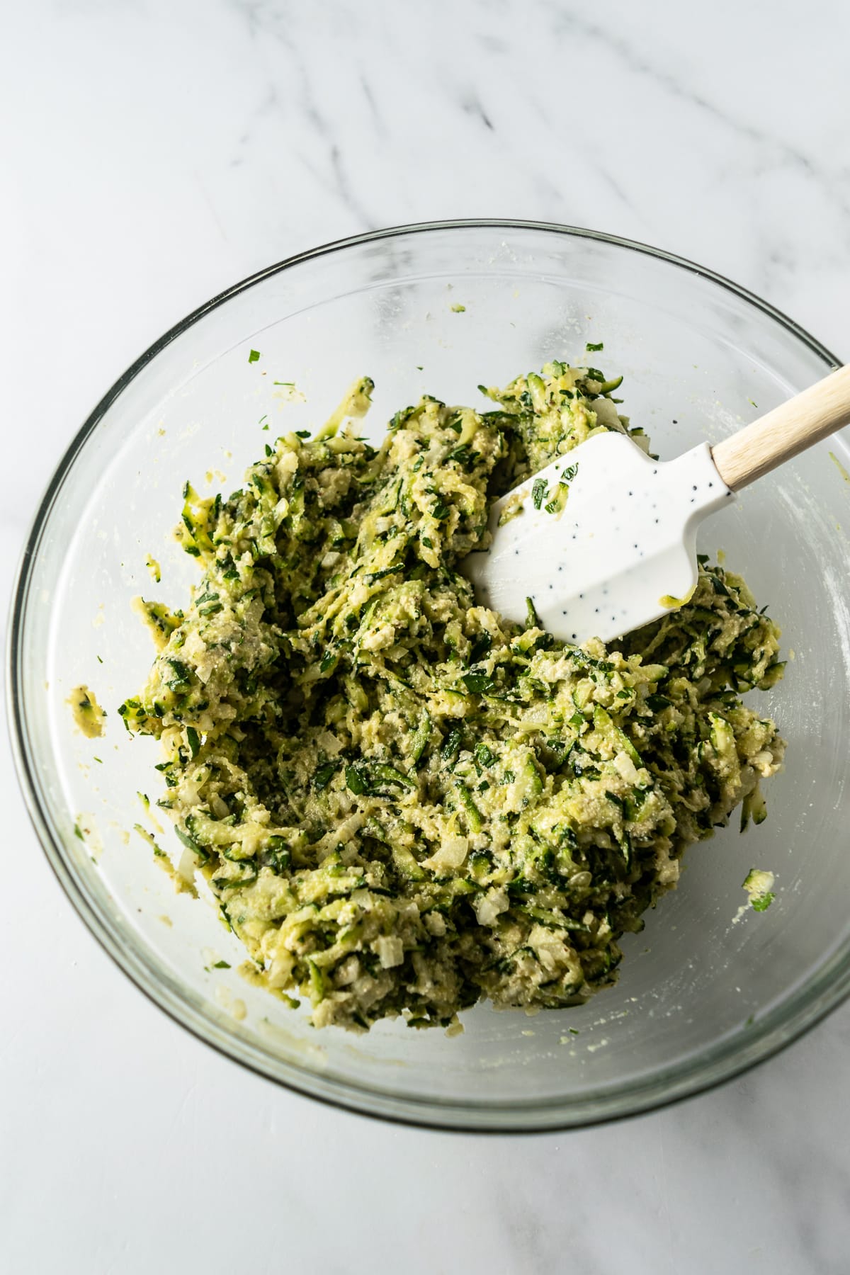 zucchini mixture in a bowl with spatula on a white table.
