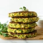 stacked zucchini fritters topped with yogurt sauce on parchment paper.