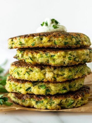 stacked zucchini fritters topped with yogurt sauce on parchment paper.