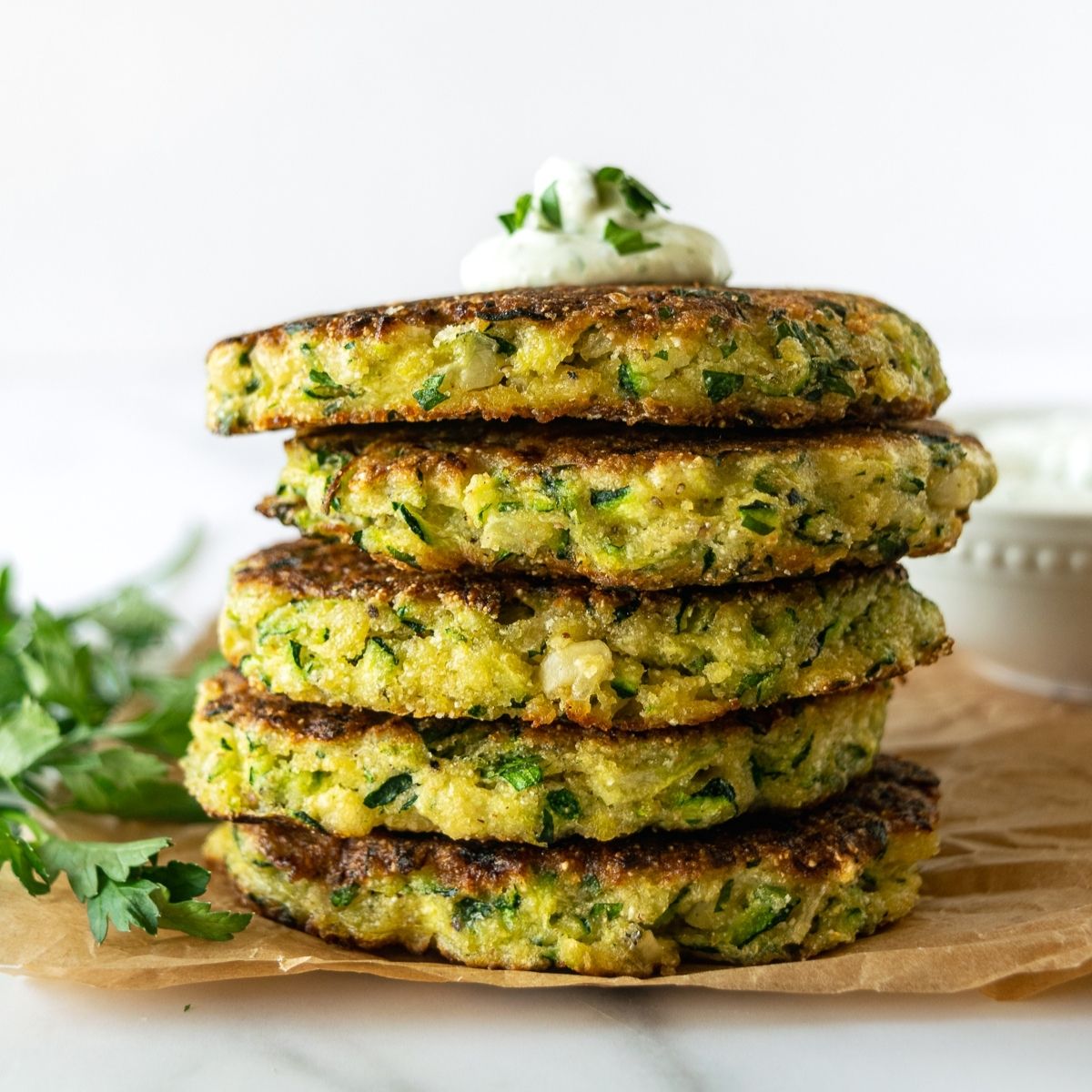 stacked zucchini fritters topped with yogurt sauce on parchment paper.