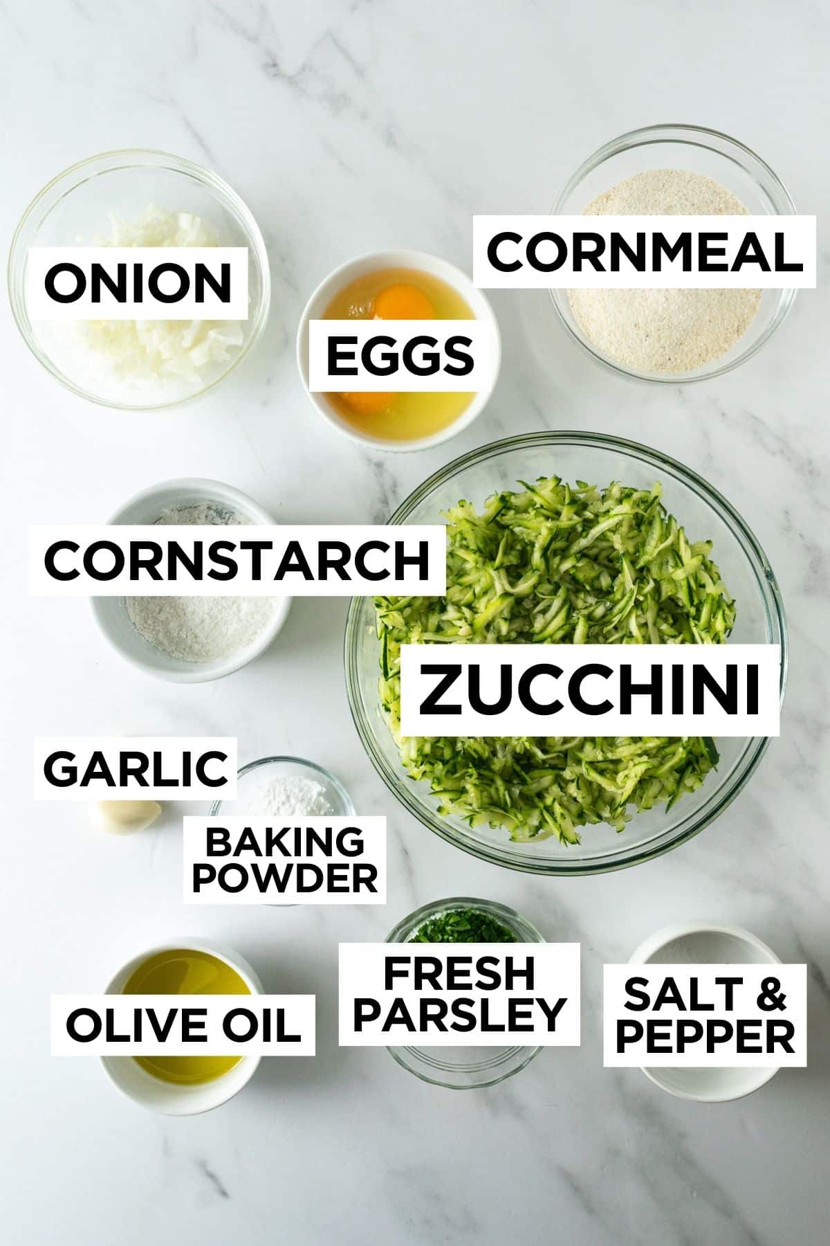 ingredients for zucchini fritters in bowls on a white table.