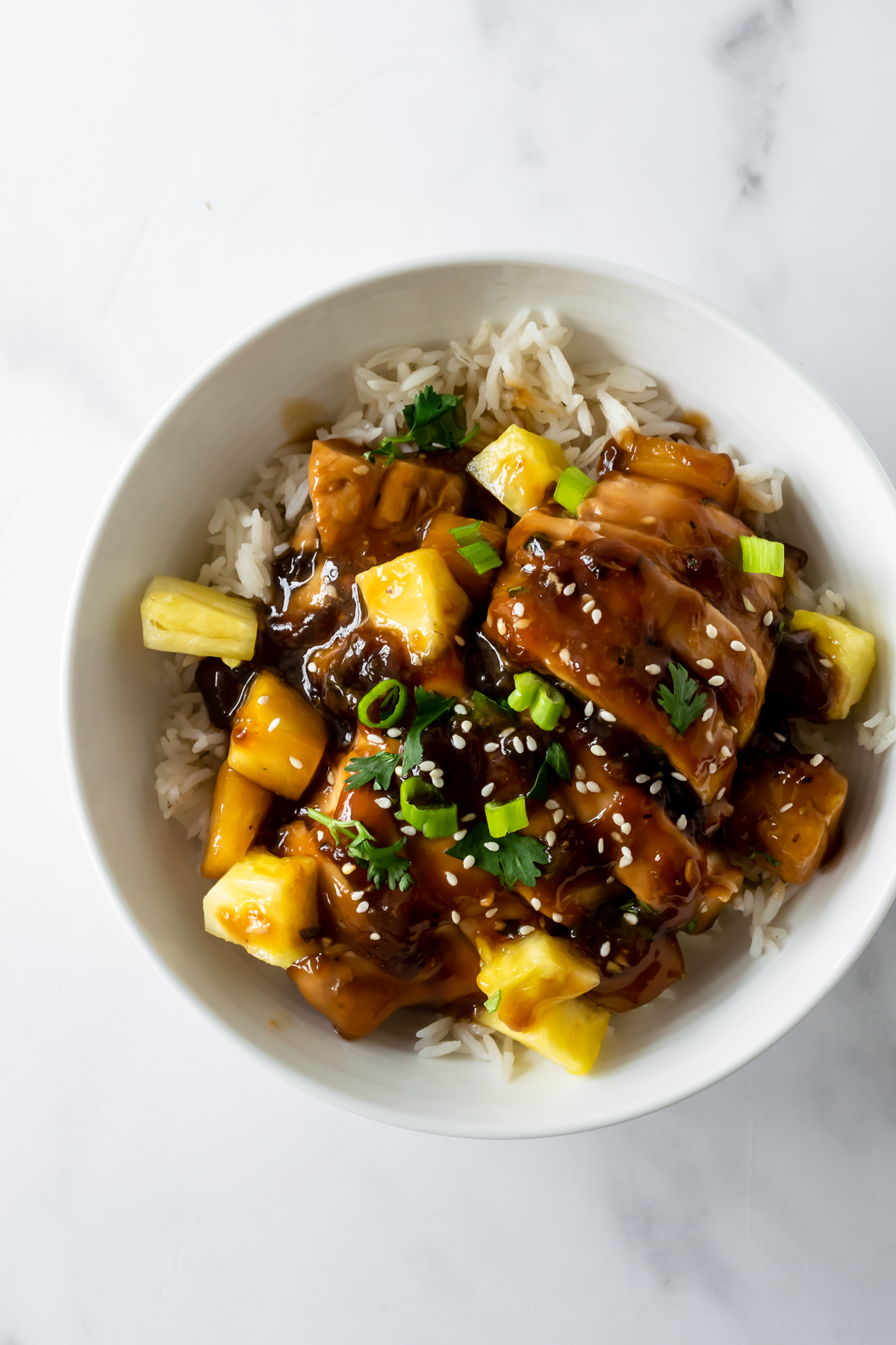 baked teriyaki chicken with pineapple in a white bowl with rice topped with sesame seeds.
