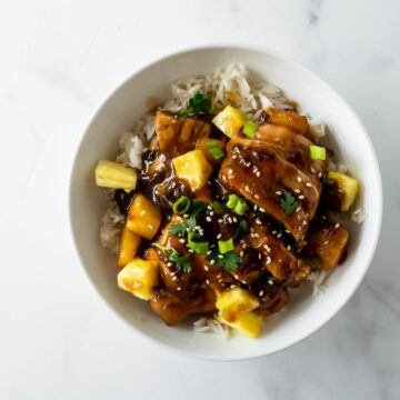 baked chicken teriyaki with pineapple in a white bowl with rice topped with sesame seeds.