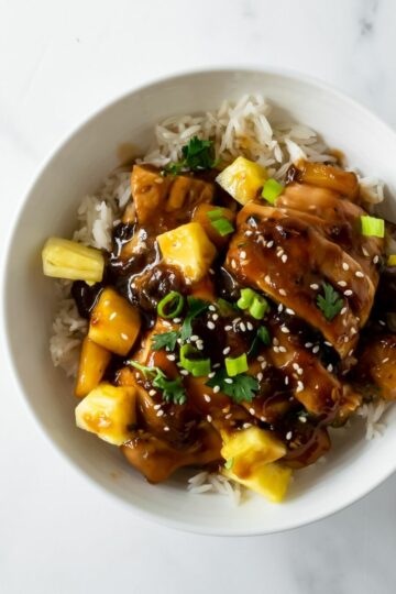 baked chicken teriyaki with pineapple in a white bowl with rice topped with sesame seeds.