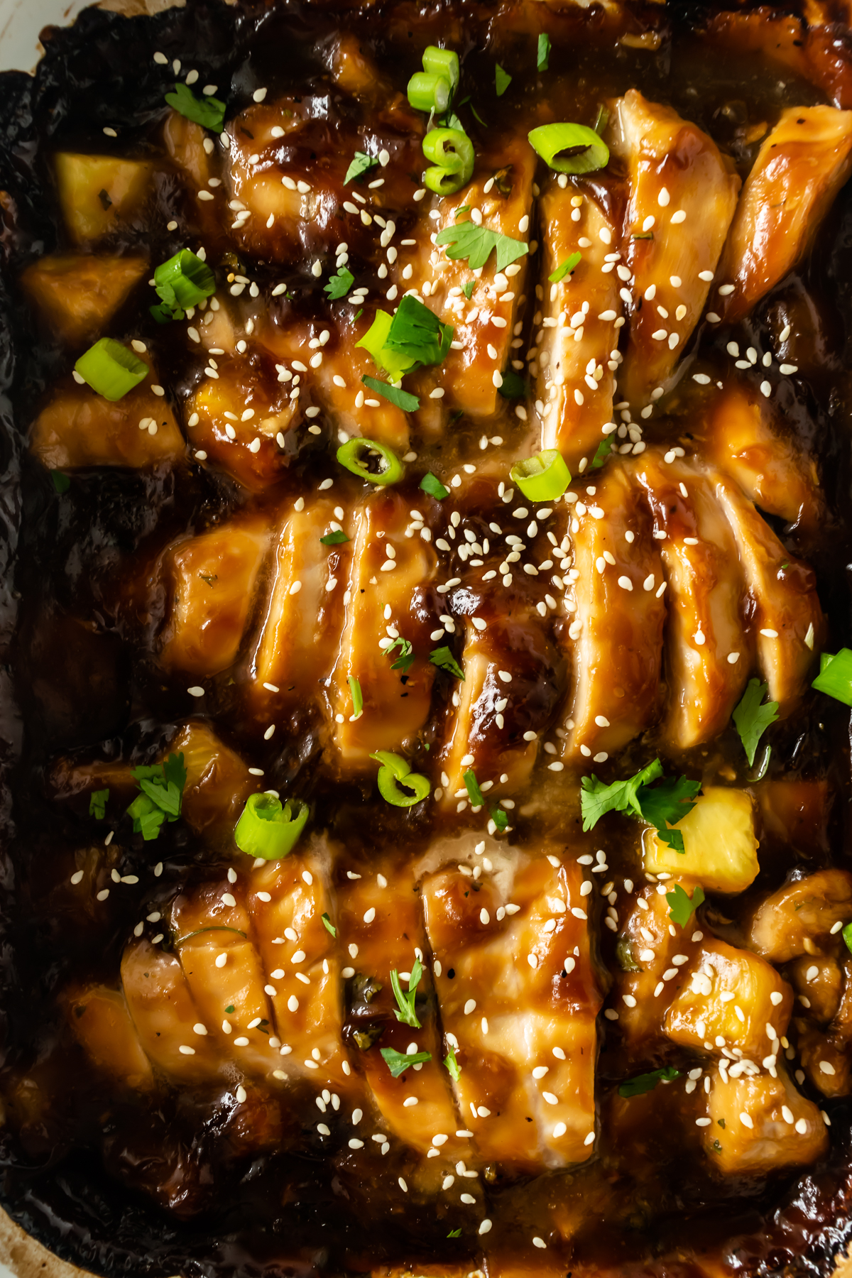 sliced baked teriyaki chicken and pineapple in a white baking dish topped with sesame seeds and green onion.