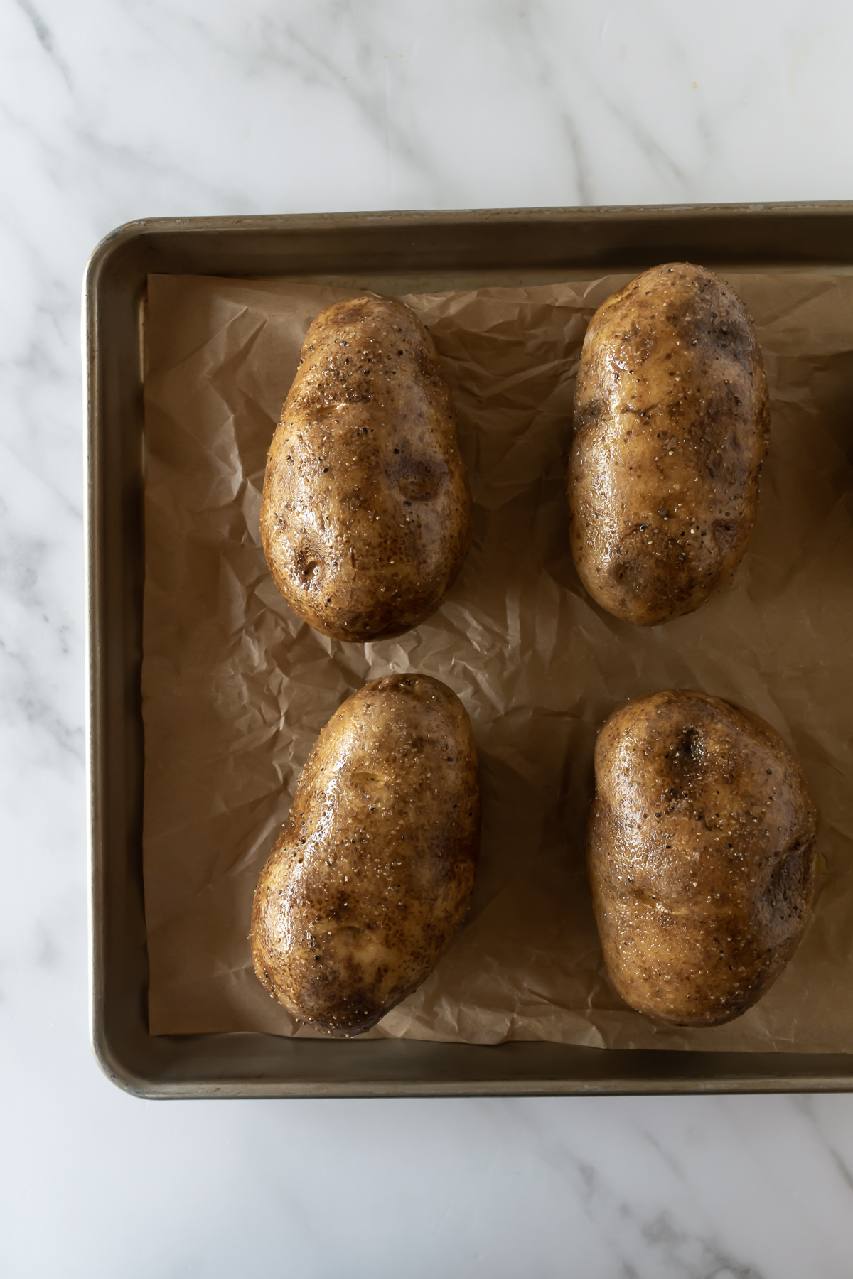 potatoes seasoned with olive oil, salt, and pepper on a baking sheet lined with parchment paper.