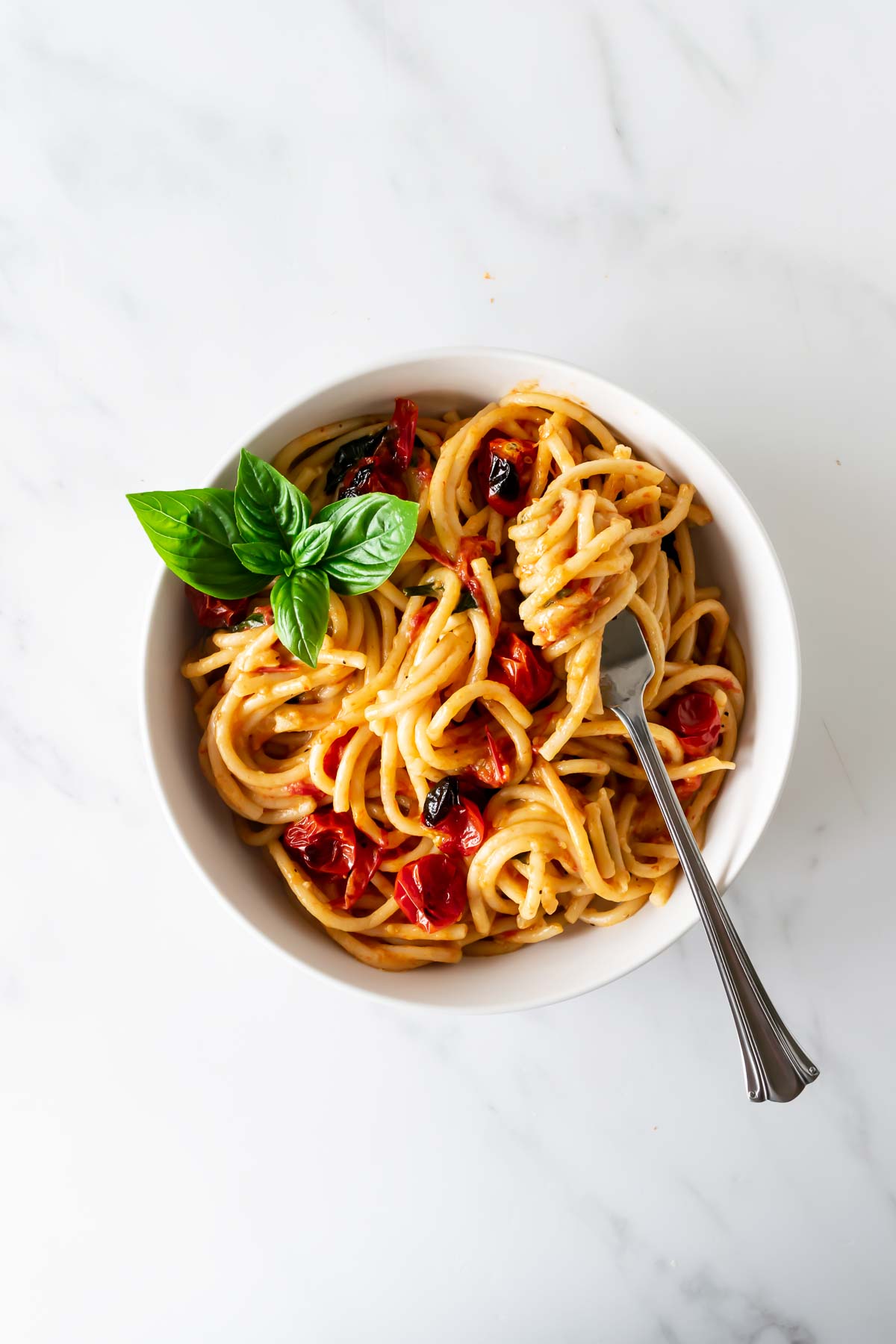 pasta with tomatoes twirled on a spoon in a white bowl garnished with basil.