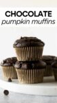 stacked chocolate pumpkin muffins on a marble board with chocolate chips with overlay text "chocolate pumpkin muffins".