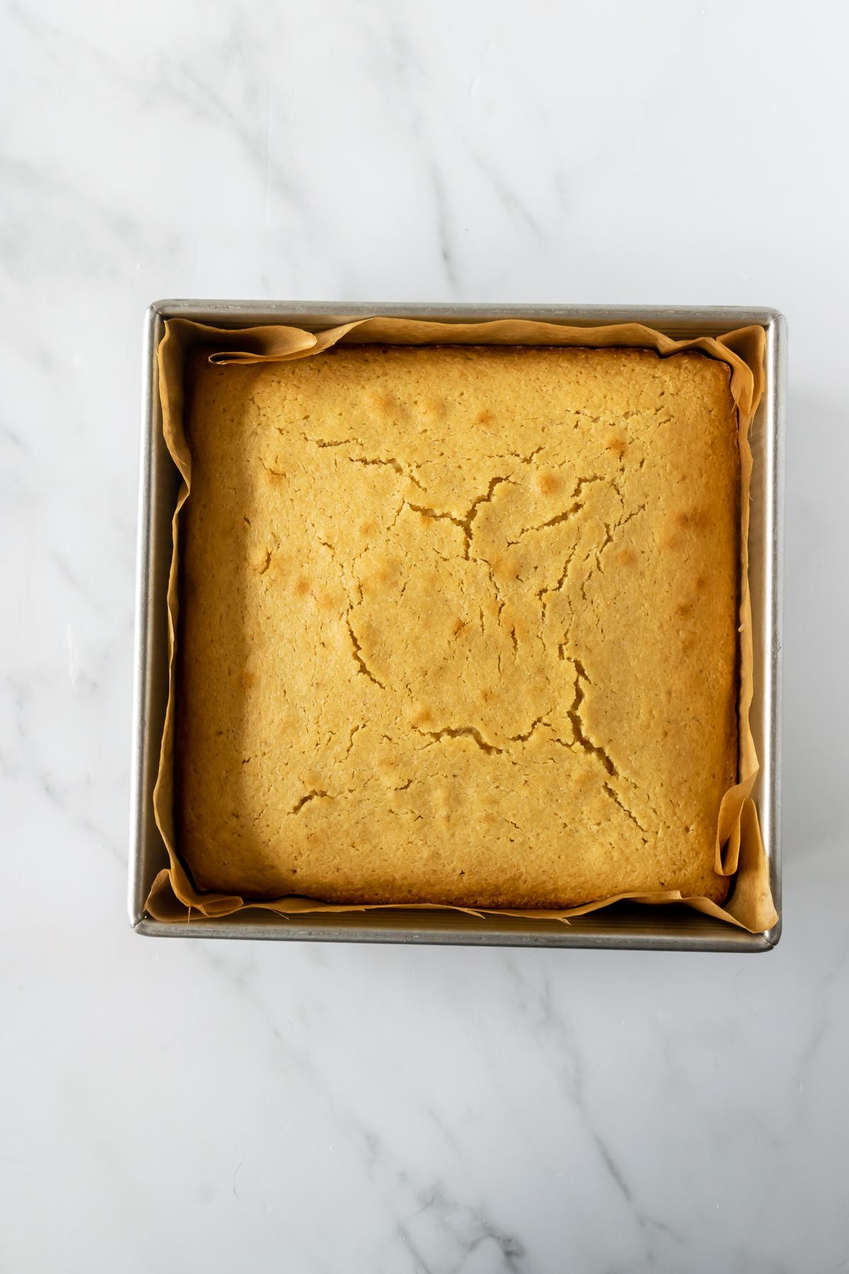 baked cornbread in a square baking pan on a white table.