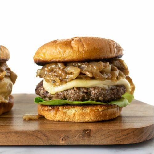 French onion burger with caramelized cheese, melted cheese and lettuce sitting on a wooden board.