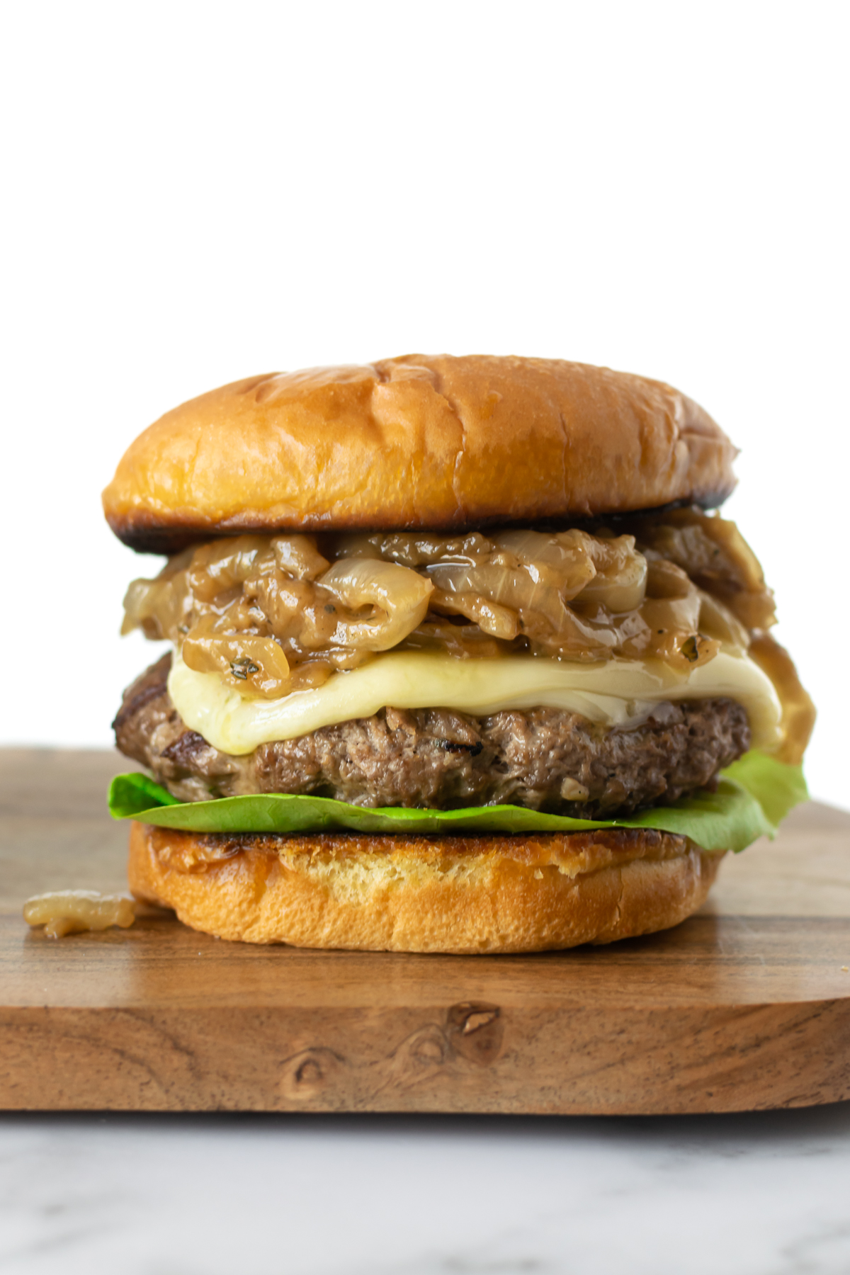 French onion burger with caramelized cheese, melted cheese and lettuce sitting on a wooden board.