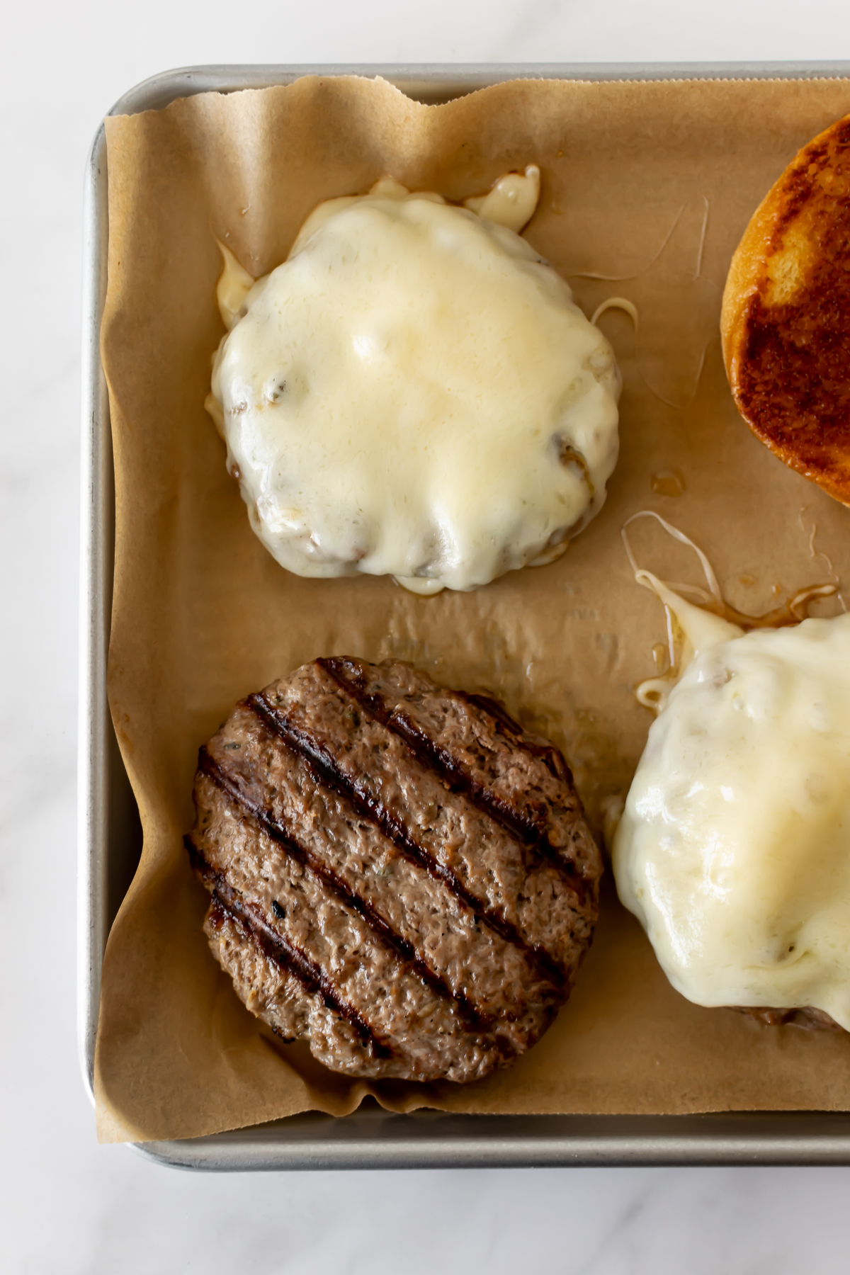 french onion burger patties topped with melted cheese on a baking sheet lined with parchment paper.