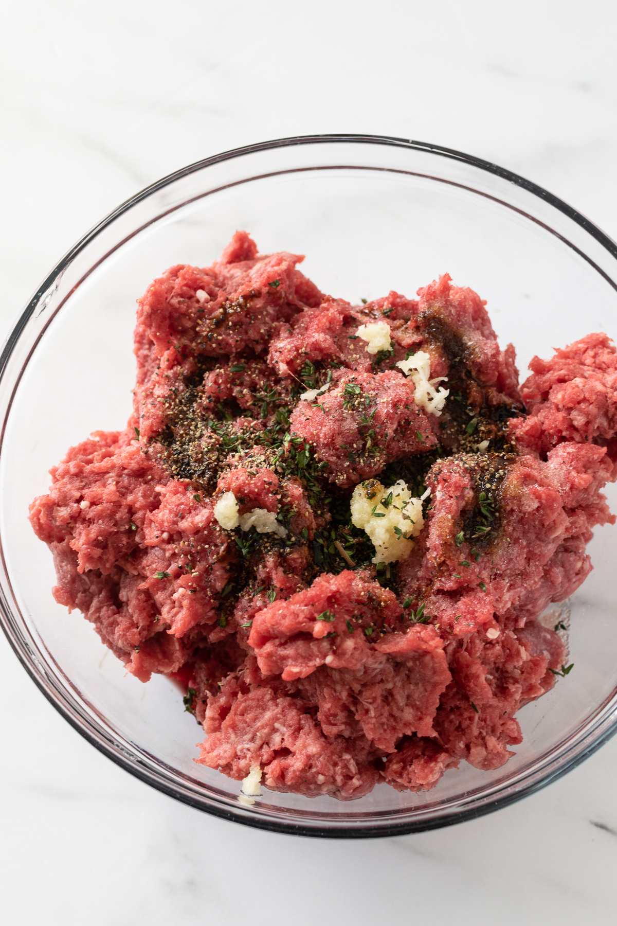 ground beef with spices in a mixing bowl on a white table.