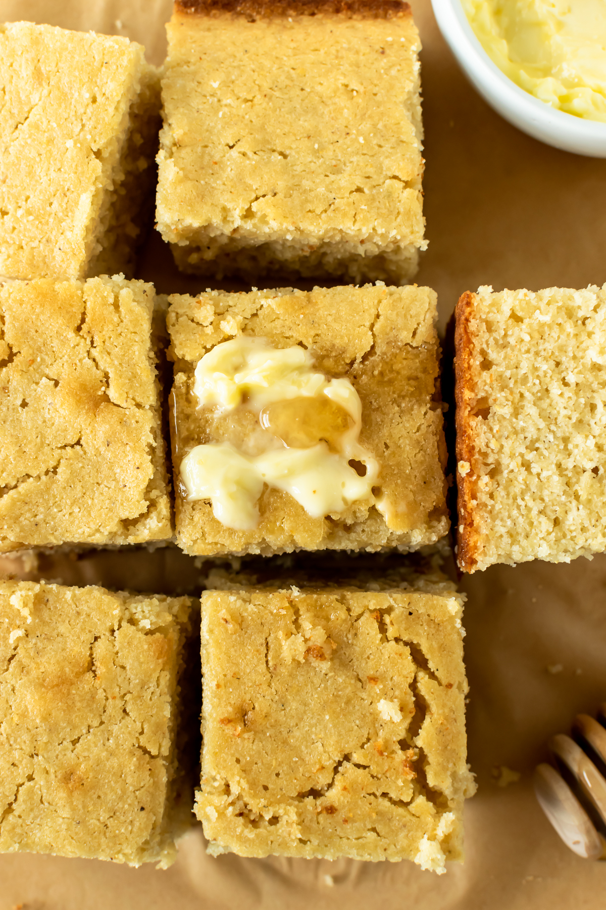 squares of homemade cornbread with a smear of butter and honey on parchment paper.