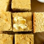 squares of homemade cornbread with a smear of butter and honey on parchment paper.