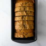 zucchini bread cut into slices in a loaf pan on a white table.