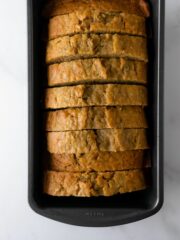 zucchini bread cut into slices in a loaf pan on a white table.