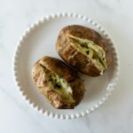 two baked potatoes on a white plate sliced open with chopped parsley.