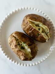 two baked potatoes on a white plate sliced open with chopped parsley.
