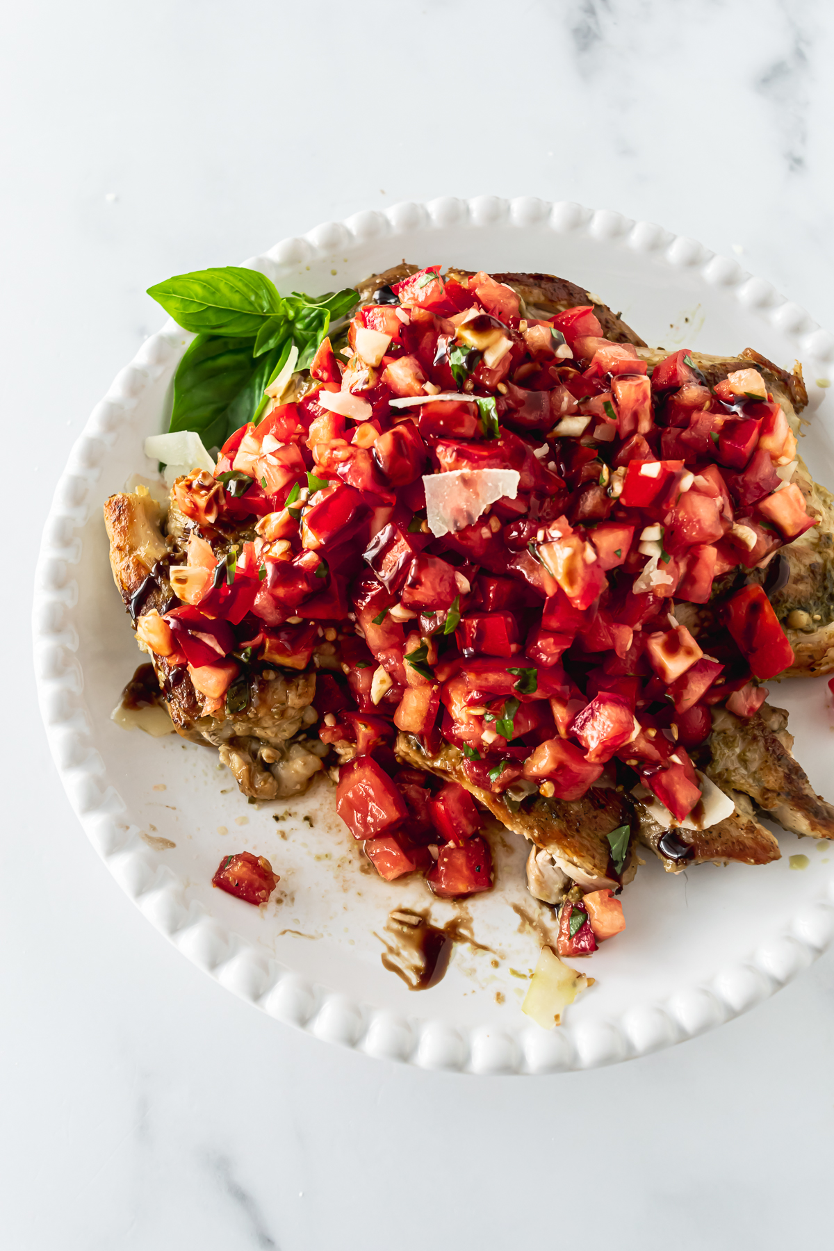 bruschetta chicken on a white plate with diced tomatoes and balsamic glaze on top.