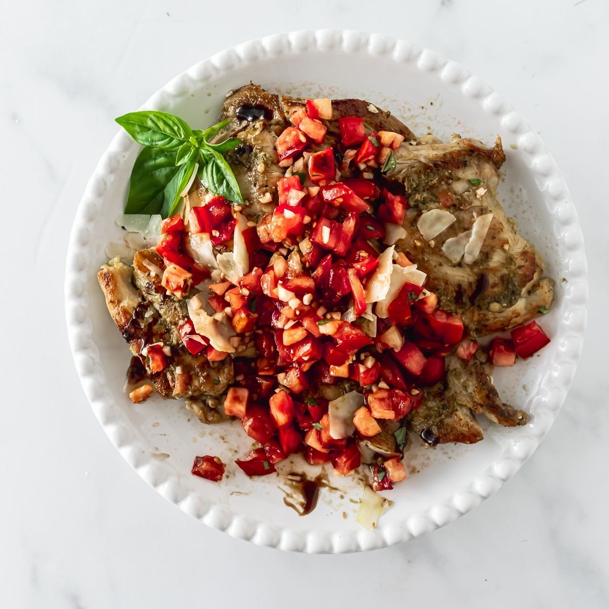 bruschetta chicken on a white plate with diced tomatoes and balsamic glaze on top.