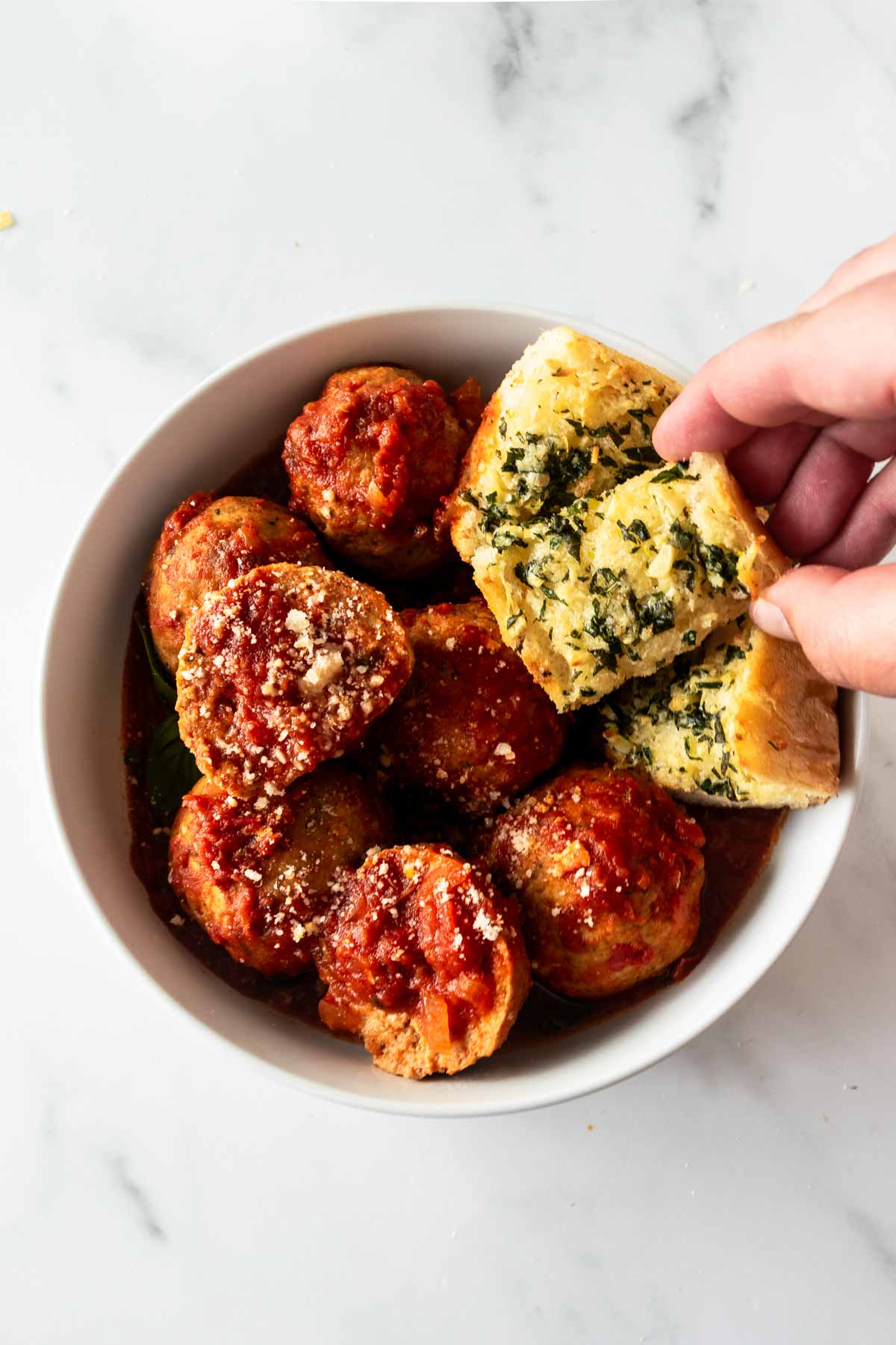 slow cooker turkey meatballs in a white bowl with a hand holding garlic bread.