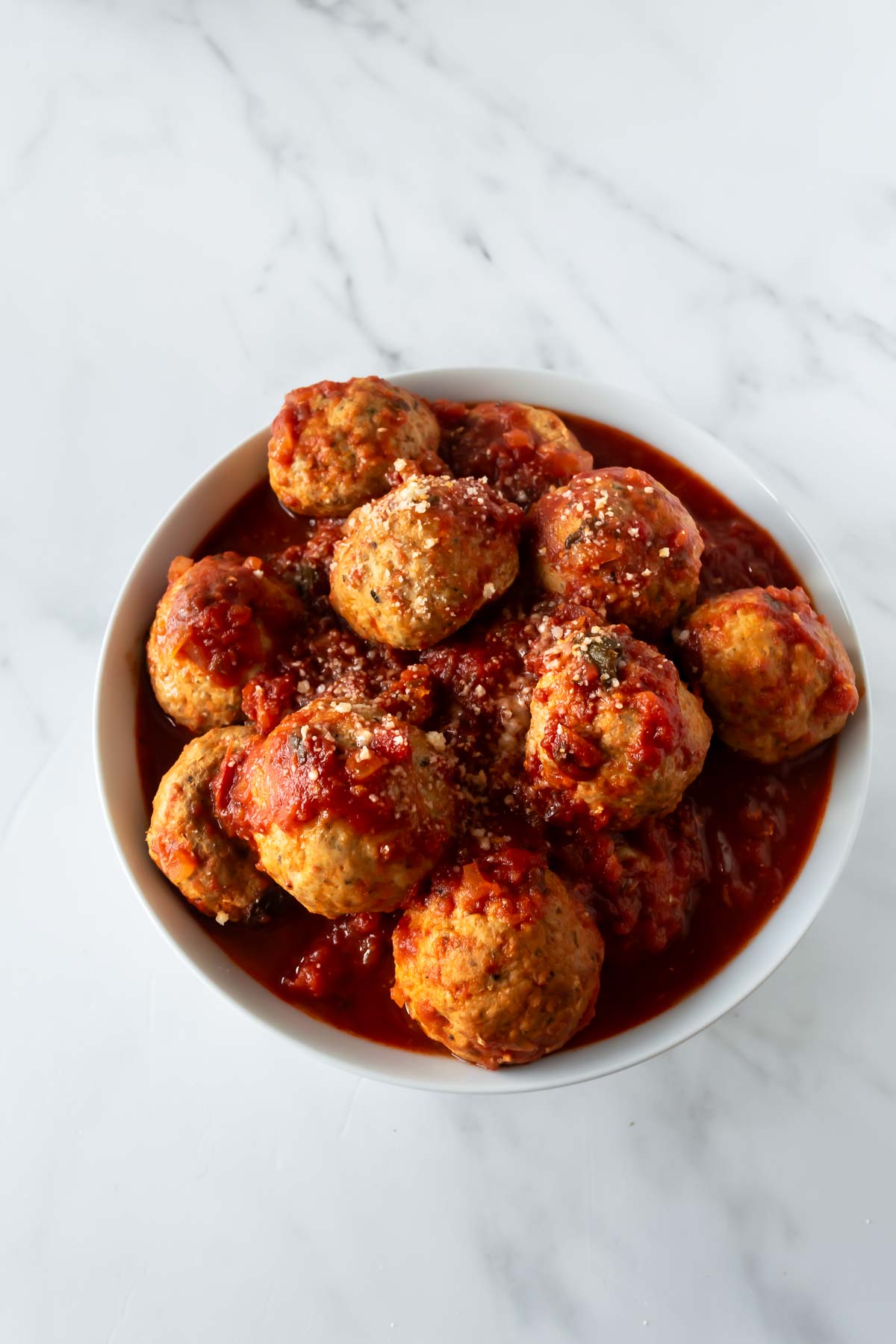 slow cooker turkey meatballs in a white bowl on a white table with marinara sauce.